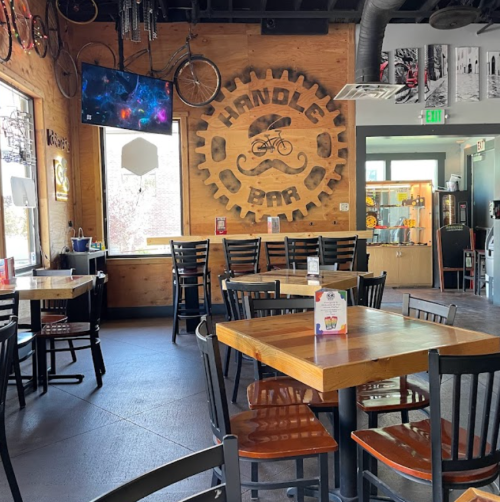 Interior of a bar with wooden walls, bike-themed decor, empty tables, and a TV displaying colorful graphics.