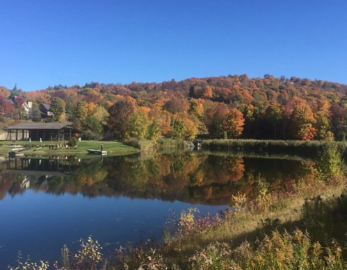 A serene lake surrounded by vibrant autumn foliage and a clear blue sky, reflecting the colorful trees.
