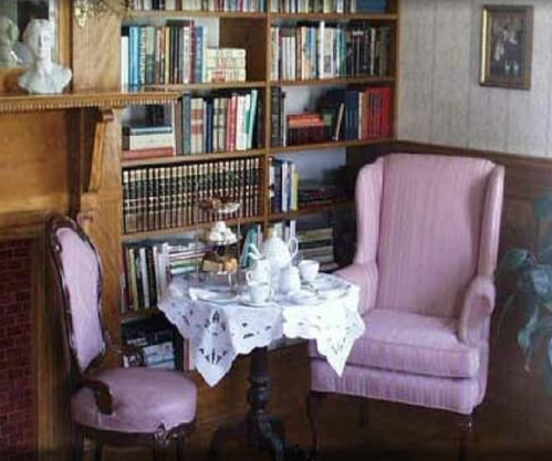 Cozy reading nook with pink chairs, a small table set for tea, and a bookshelf filled with books in the background.