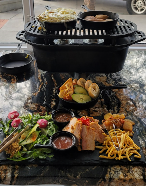 A table with a variety of dishes, including grilled meats, vegetables, and sides, served on a black stone platter.