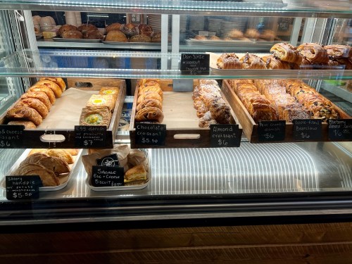 A display case filled with various pastries, including croissants, danishes, and sweet rolls, with price tags.