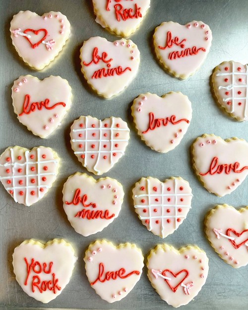 A tray of heart-shaped cookies decorated with pink icing and red messages like "be mine" and "you rock."