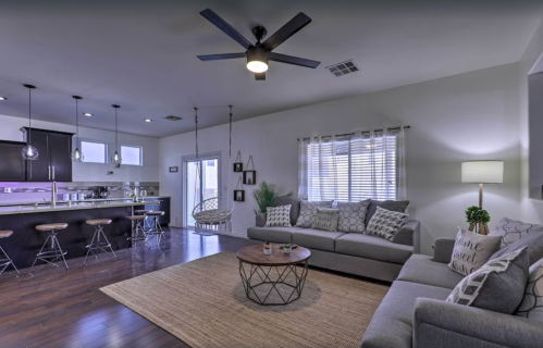A modern living room with gray sofas, a round coffee table, and a kitchen in the background, featuring a swing chair.