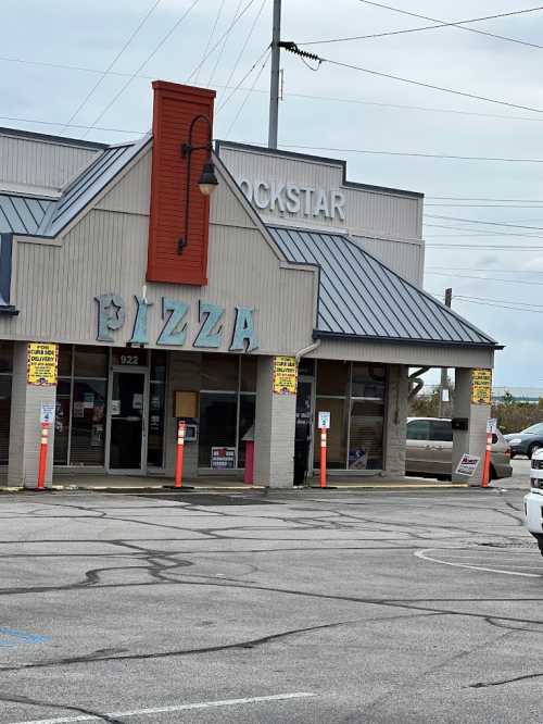 A pizza restaurant with a colorful sign, located in a commercial area with parking spaces and cloudy skies.