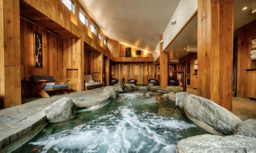 A serene spa interior featuring wooden walls, a stone-lined pool, and relaxing seating areas.