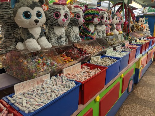 A colorful carnival booth with plush toy cats and bins filled with various candies and treats.