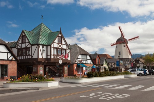 Charming town square featuring a Dutch-style windmill and Tudor-style buildings under a blue sky.