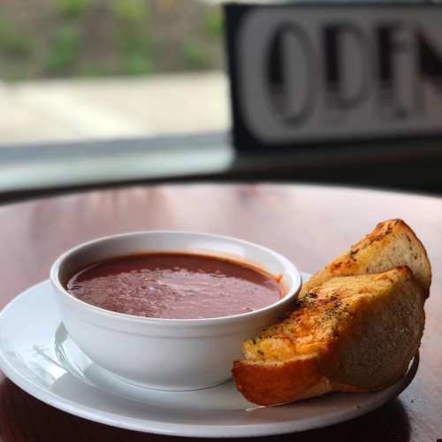 A bowl of tomato soup served with two slices of toasted garlic bread on a white plate.