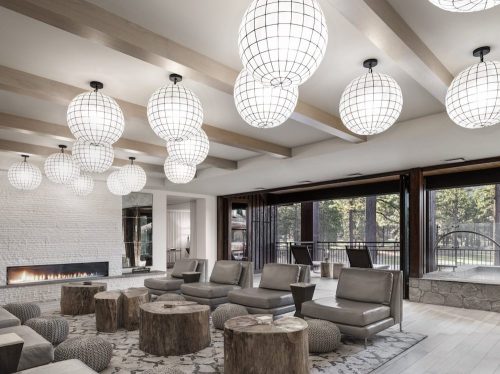 Modern lounge with large globe lights, comfortable seating, and a stone fireplace, surrounded by large windows.