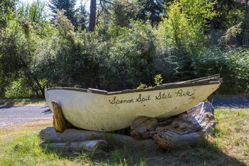 A weathered boat rests on logs in Spencer Spit State Park, surrounded by lush greenery and trees.