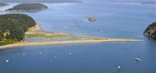 Aerial view of a serene coastal landscape with sandy beaches, green forests, and boats on calm blue waters.