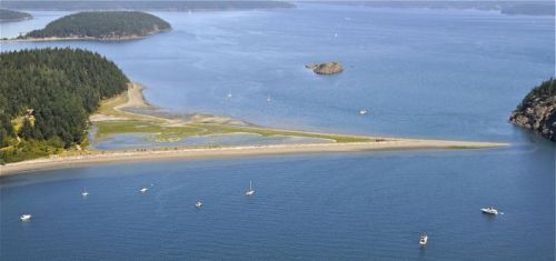 Aerial view of a serene coastal landscape with sandy beaches, green forests, and boats on calm blue waters.