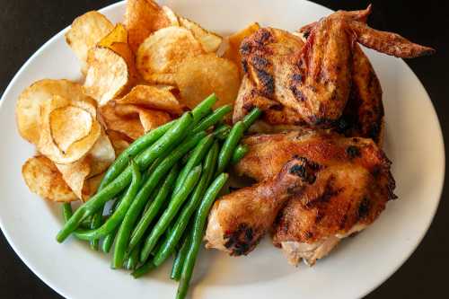 Grilled chicken with crispy potato chips and green beans on a white plate.