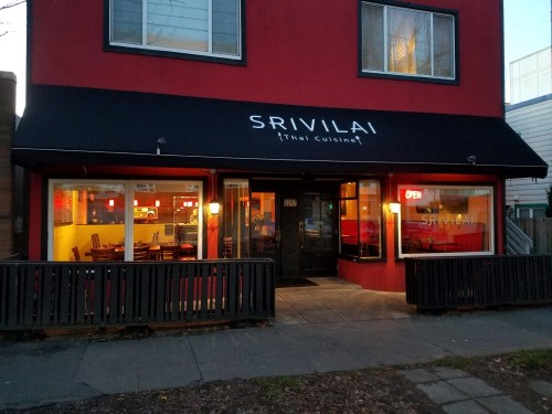 Exterior of Srivilai Thai Cuisine restaurant, featuring a red building, open sign, and outdoor seating area.