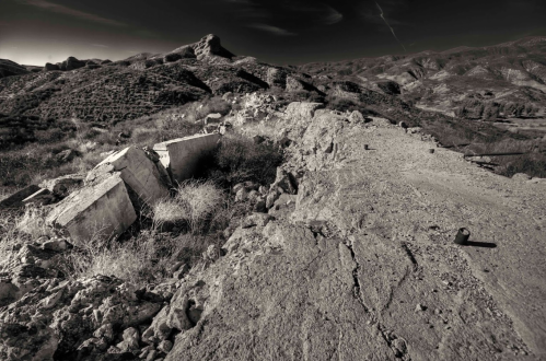 A desolate landscape with crumbling concrete remnants and rocky terrain under a dramatic sky.