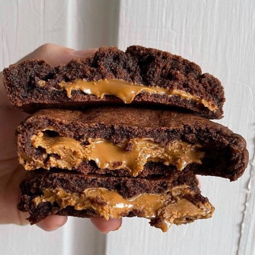 A hand holding three layers of chocolate cookies filled with creamy caramel or peanut butter.