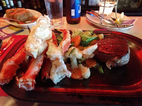 A sizzling plate featuring a steak, crab legs, and a medley of vegetables including broccoli and carrots.