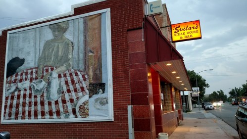 Exterior of Guitars Steak House & Bar, featuring a mural of a woman sitting at a table with a checkered tablecloth.