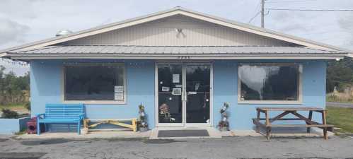 A light blue building with a welcoming entrance, featuring a picnic table and colorful seating outside.