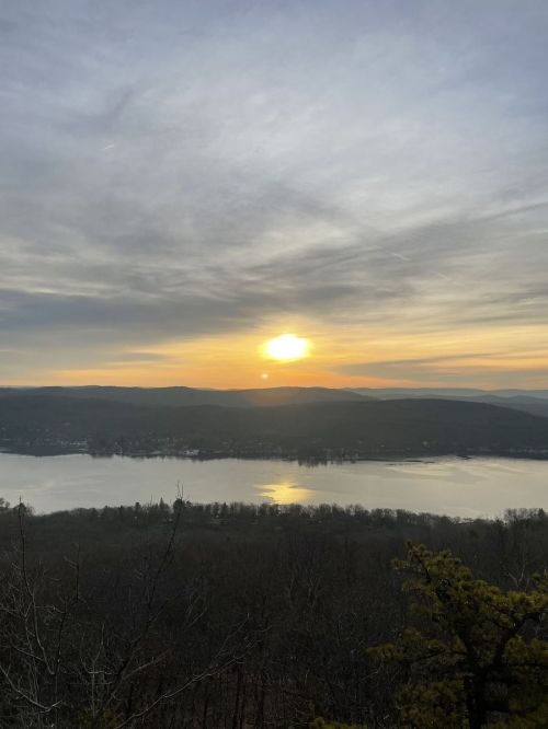 A serene sunset over a lake, with soft clouds and distant hills reflecting warm colors on the water.
