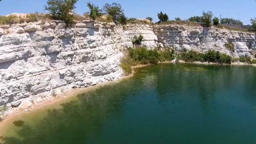 A serene lake bordered by white cliffs and greenery under a clear blue sky.