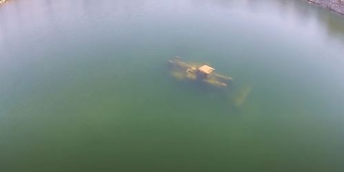 An underwater structure partially submerged in a greenish lake, with ripples on the water's surface.