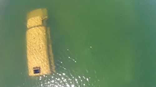 Aerial view of a submerged structure in clear green water, partially visible above the surface.