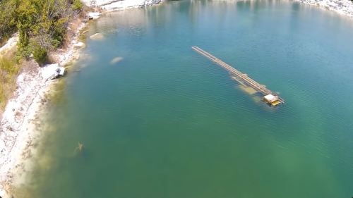 Aerial view of a calm lake with a small boat and visible underwater structures near the shore.