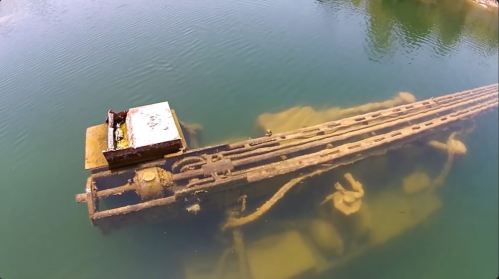 An underwater view of a rusted, submerged structure with machinery, partially visible in clear water.