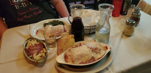 A table setting with two plates of pasta, a glass of wine, water, and bread, in a restaurant.