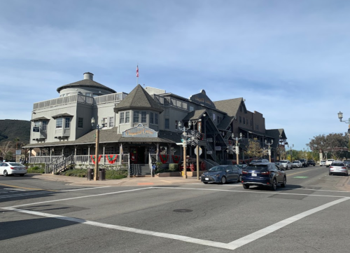 A charming multi-story building with a round roof, located at a street intersection, surrounded by trees and parked cars.