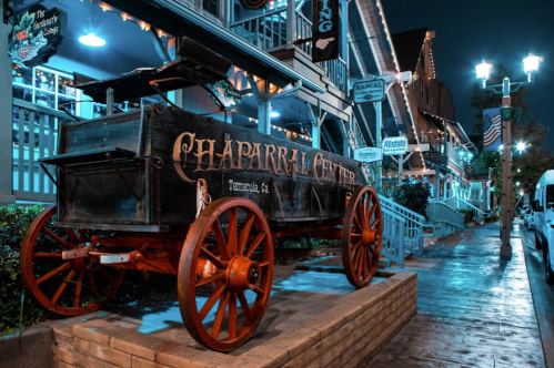 A vintage wagon with "Chaparral Center" signage, illuminated by blue lights, on a charming street at night.