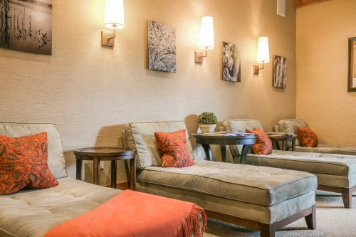 Cozy lounge area with two chaise lounges, decorative pillows, side tables, and wall art in warm tones.