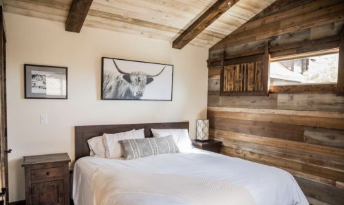 Cozy bedroom with a wooden accent wall, a large bed, and a framed cow portrait above the headboard.