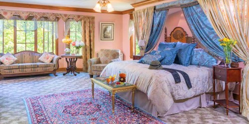 Cozy bedroom with a large bed, elegant curtains, a floral sofa, and a decorative rug, surrounded by natural light.