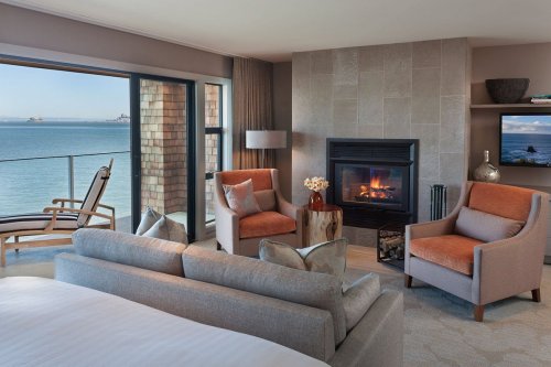 Cozy hotel room with a fireplace, ocean view, and modern furnishings, featuring a sofa and two armchairs.
