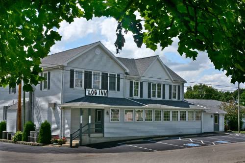 A white, two-story building with "Log Inn" sign, surrounded by greenery and a clear blue sky. Parking area in front.