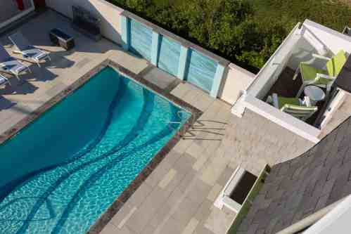 Aerial view of a modern pool with lounge chairs and a balcony overlooking greenery.