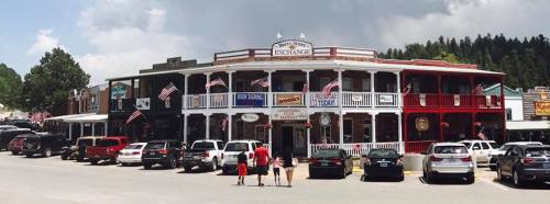 Historic building with multiple shops, American flags, and parked cars in a small town setting. Trees in the background.