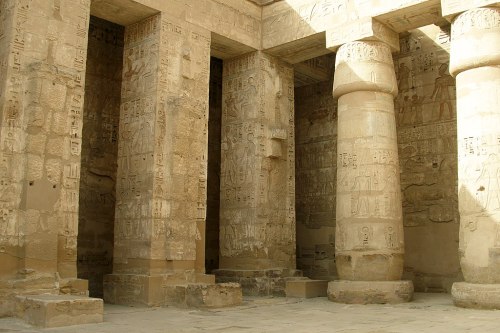Ancient stone columns with intricate hieroglyphics in a sunlit temple interior.