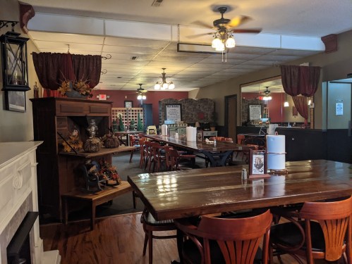 Cozy restaurant interior with wooden tables, chairs, and a fireplace, featuring warm lighting and autumn decorations.