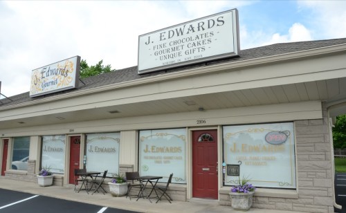 Exterior of J. Edwards shop featuring fine chocolates, gourmet cakes, and unique gifts, with an "Open" sign in the window.
