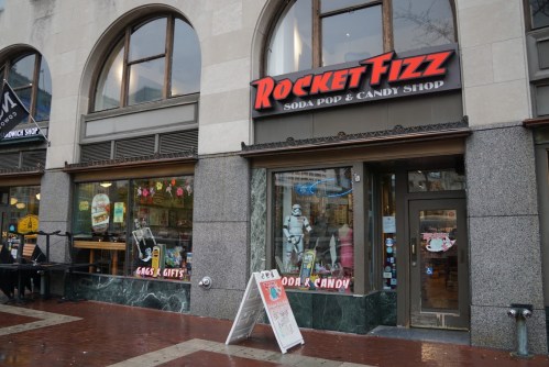 Exterior of Rocket Fizz, a soda pop and candy shop, featuring a colorful sign and a display of gifts and treats.