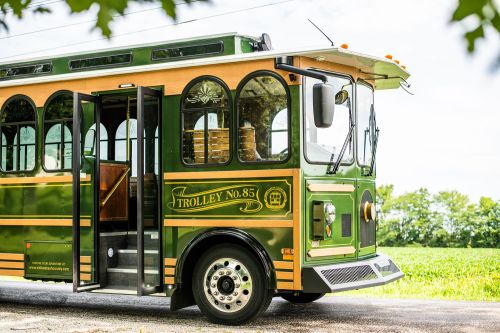 A vintage green trolley bus with open doors parked on a scenic road surrounded by greenery.