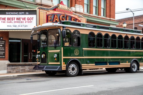 A green trolley bus parked in front of a theater marquee displaying "The Best We've Got" show details.
