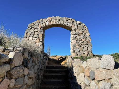 Stone archway with steps leading up, set against a clear blue sky.