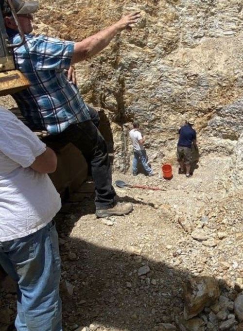 Three people working in a rocky excavation site, with one person pointing and two others digging.