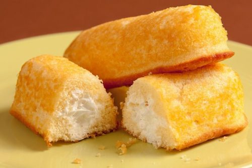 Three golden Twinkies on a yellow plate, one cut in half to reveal its creamy filling.