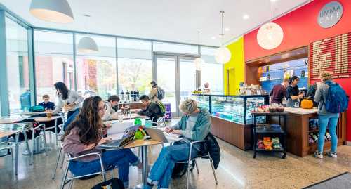 A busy café with students studying, a counter displaying snacks, and colorful walls.