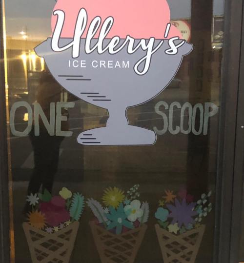 Sign on a window for "Ullery's Ice Cream" featuring a sundae graphic and the text "One Scoop" with colorful ice cream cones below.